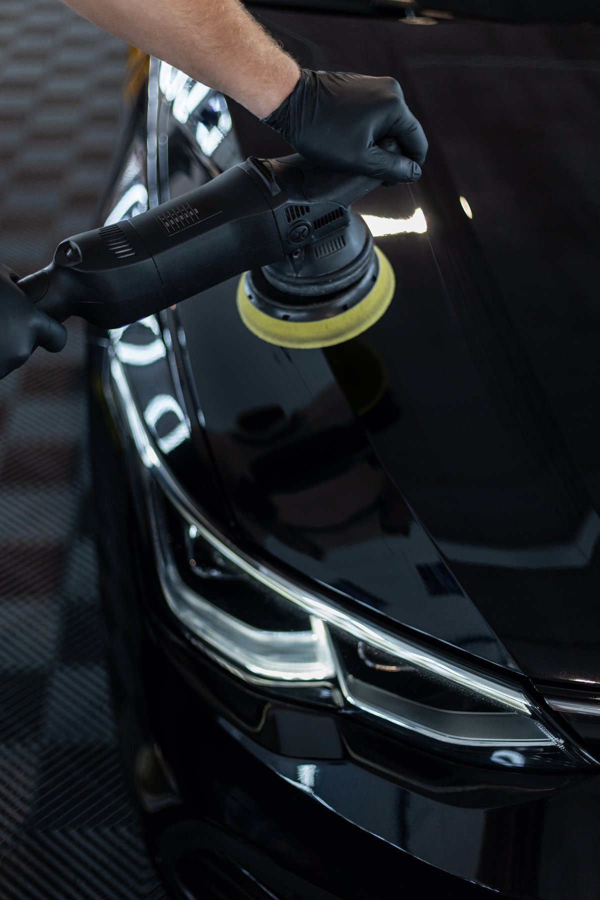 Professional polishing a black car in a garage, scratch removal